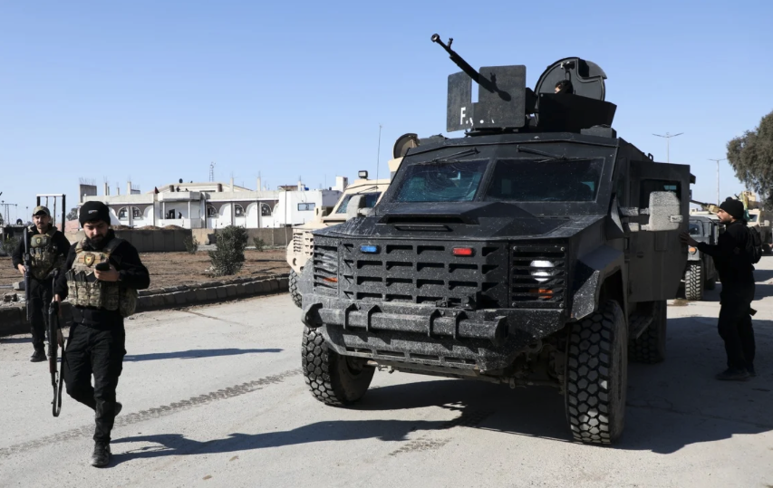 Members of the Syrian Democratic Forces walk near an armoured vehicle following clashes between SDF and Syrian government forces, in Hasakah, Syria,